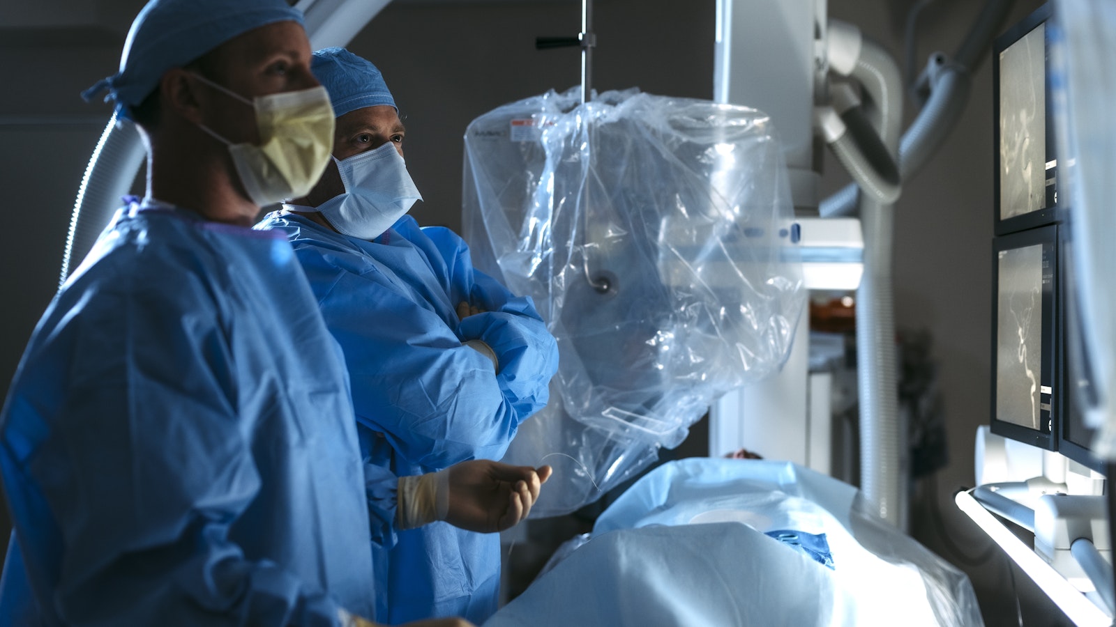 Two doctors standing in a surgery room looking at image guided surgery with patient in foreground